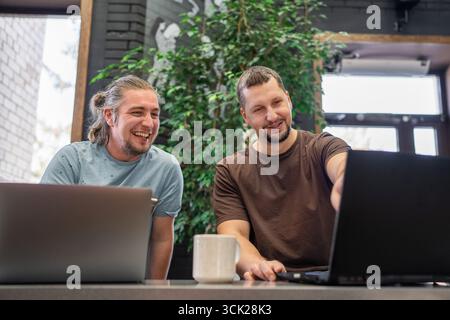 Two laughing It Software engineers working on project and programming in coffee shop. Successful start up project concept. Stock Photo