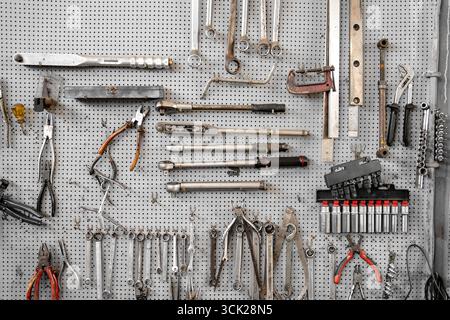 Various wrenches and hand tools hanging on pegboard in workshop. Neatly organized tools include combination wrenches, pliers, and adjustable wrenches for mechanical work  Stock Photo