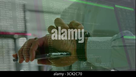 IT pro's hand pointing stylus at tablet in IT office, with smartwatch and monitors displaying code Stock Photo