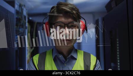 Operating servers and monitoring data charts, data center technician in yellow vest and headphones Stock Photo