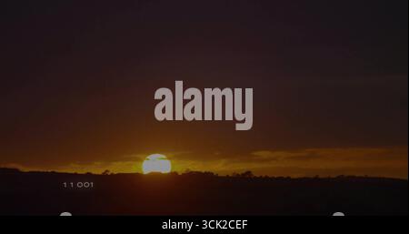 Sinking sun disc glowing over hills at rural landscape, showing silhouetted shrubs, numeric 11 001 Stock Photo