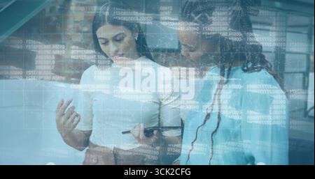 Two coworkers in business attire analyzing code overlay on tablet with stylus in open-plan office Stock Photo