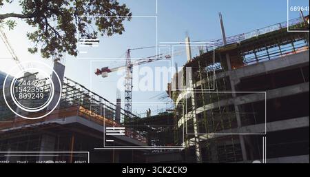 Standing construction workers wearing helmets vests on scaffolding at job site, with tower crane Stock Photo