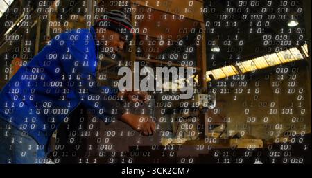 Operating machinist wearing ear protection adjusting lathe controls in workshop, binary overlay Stock Photo