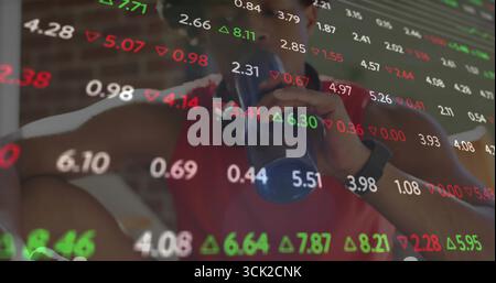 Drinking man wearing black watch sipping from blue shaker bottle in gym, with stock ticker overlay Stock Photo