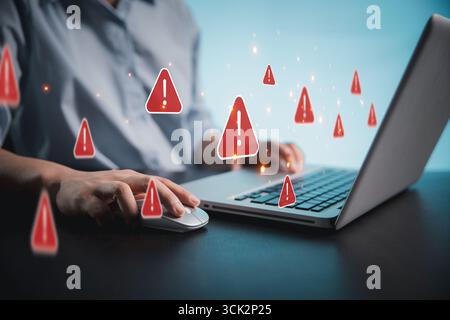 Person using phone and laptop is shown online with red warning signs indicating potential security threats. Cybersecurity technology, system warning o Stock Photo
