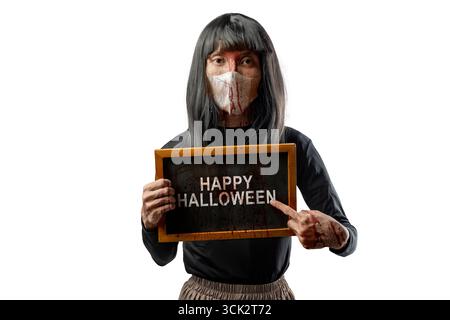 Indonesian southeast asian transgender man dressed as a woman wearing a bloody face mask and showing the text of Happy Halloween on a blackboard. Conc Stock Photo