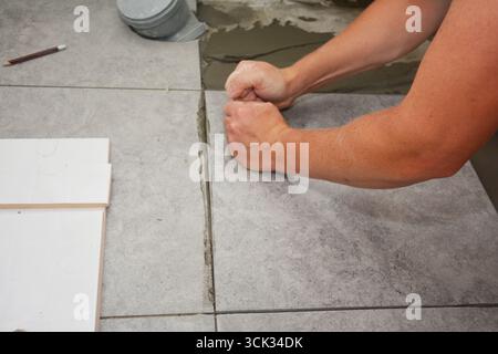 Bathroom flooring works. Worker installing ceramic tile on the floor. Stock Photo