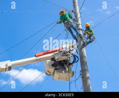 a team of electricians installs high-voltage electrical wires on poles Stock Photo