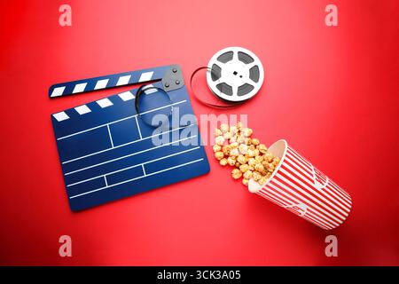 Blue clapperboard, film reel and popcorn on red background, flat lay Stock Photo