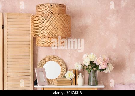 Bedside table with mirror, books and beautiful peonies in bedroom Stock Photo