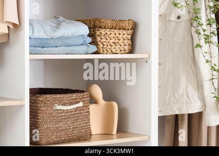 Wicker organizers with clothes on shelves in wardrobe Stock Photo