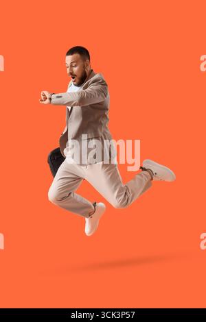 Surprised young businessman checking time while jumping on orange background Stock Photo