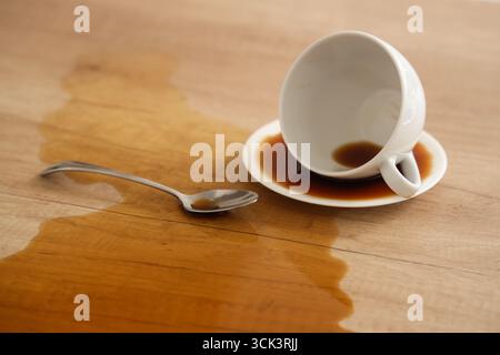 Overturned cup with spoon and spilled coffee on table in kitchen, closeup Stock Photo
