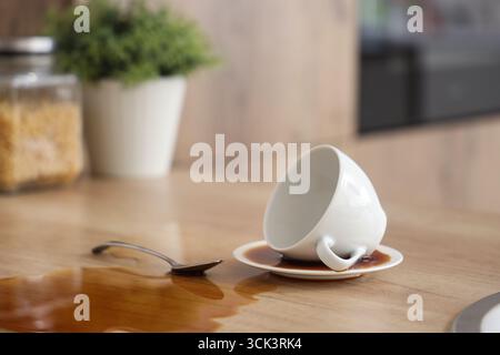 Overturned cup with spoon and spilled coffee on table in kitchen, closeup Stock Photo