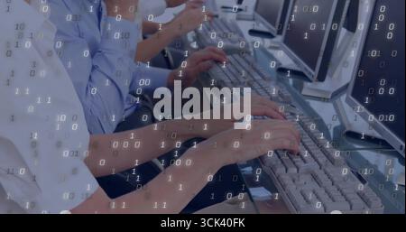 Typing office workers entering program commands at long office desk, with keyboards and monitors Stock Photo