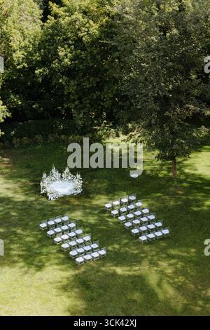 A serene outdoor location boasts neatly arranged chairs, giving a romantic ambiance for a wedding celebration under lush trees. Stock Photo