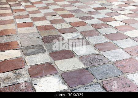 Cobblestone pavement featuring rough textured surfaces of red, white and gray blocks. Background photo texture Stock Photo