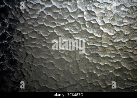 Close-up view of textured glass surface is creating an abstract pattern with interplay of light and shadow, forming a visually interesting background Stock Photo