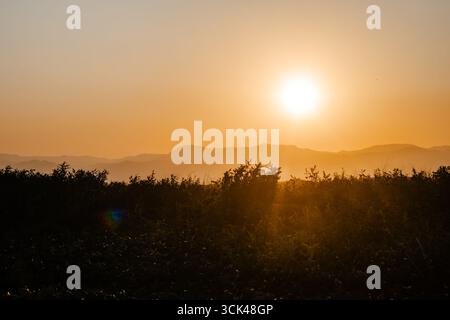 Aerial view of the sun setting behind distant mountains, casting a golden glow over the landscape, Soppeng, Sulawesi Selatan, Indonesia. Stock Photo