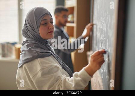 Young Adult Middle Eastern Woman Writing on Blackboard in Language Class Stock Photo
