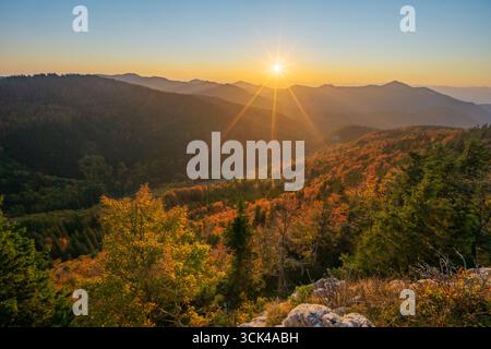 View of the sun's radiant rays kissing the autumn-painted Velka Fatra mountains, creating a symphony of colors and shadows, Blatnica, Žilina Region, S Stock Photo