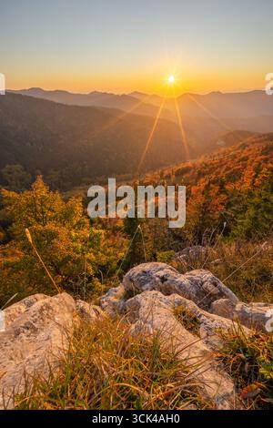 View of a radiant sunset casting long shadows over the autumn-tinged Velka Fatra mountains, with rocky outcrops in the foreground, Blatnica, Žilina Re Stock Photo