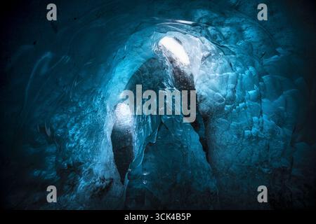 View of a mesmerizing ice cave interior with vibrant blue hues and textures, illuminated by a single natural skylight, Iceland, Iceland. Stock Photo