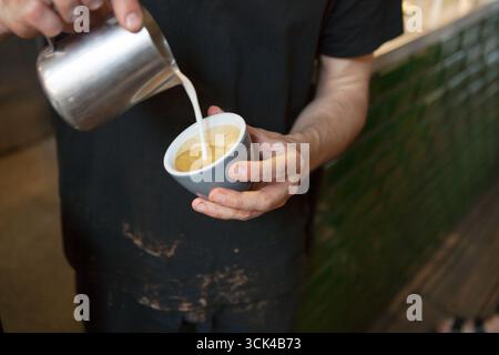 Barista pouring milk into a coffee cup in a coffee shop Stock Photo