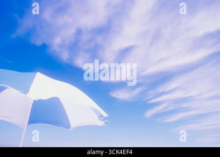 White clouds on blue sky above white and blue beach umbrella Stock Photo