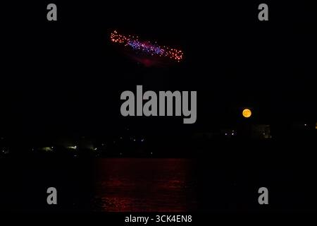 Night Sky Display with Fireworks, Full Moon, and Calm Reflections on Water Stock Photo