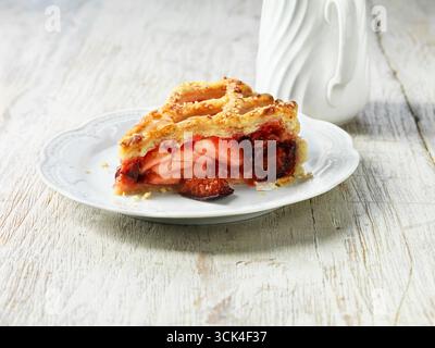 Apple, plum and raspberry pie on white plate, white jug, white washed wooden table Stock Photo