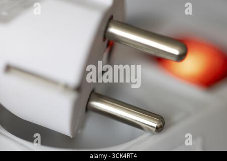 White power plug resting on a multiple socket with red indicator light, close-up of the contact pins, symbolic image for electrical energy and power c Stock Photo