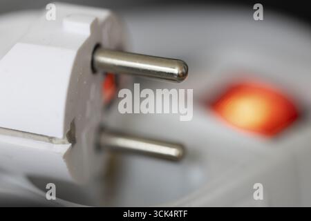 White power plug resting on a multiple socket with red indicator light, close-up of the contact pins, symbolic image for electrical energy and power c Stock Photo