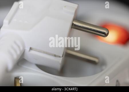 White power plug resting on a multiple socket with red indicator light, close-up of the contact pins, symbolic image for electrical energy and power c Stock Photo
