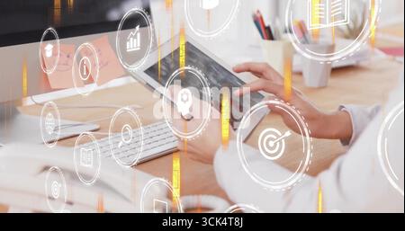 Tapping woman holding tablet at desk, with keyboard, monitor with pink sticky note and pencil cup Stock Photo