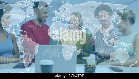 Collaborating professionals standing around table in office, with laptop tablet world map overlay Stock Photo