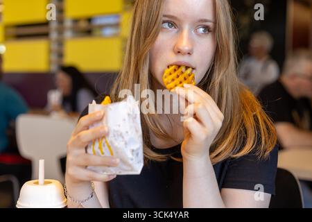 Kerpen, Germany - August, 9, 2025: Young woman eating waffle fries at McDonalds restaurant Stock Photo