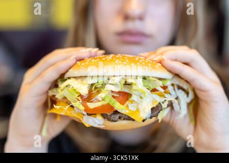 A person holds a delicious hamburger packed with fresh ingredients, including lettuce, tomato, and cheese. The setting appears to be a casual dining e Stock Photo