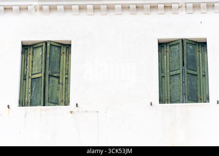 Two windows with green wooden shutters on the white fa ade of an old house Stock Photo