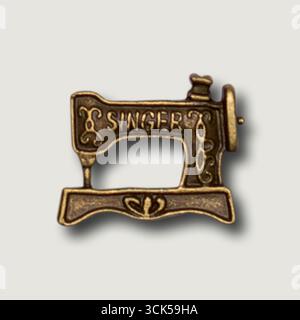 A decorative metal pin shaped like a vintage sewing machine, symbolizing sewing and craftsmanship. Stock Photo