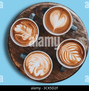 A wooden tray holds four cups of latte art coffee, showcasing intricate designs in the froth. Stock Photo