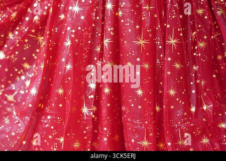 A close-up of shimmering red tulle fabric decorated with golden star patterns Stock Photo
