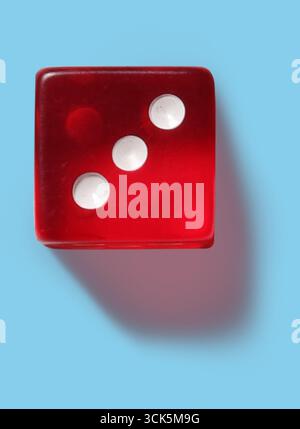 A red dice showing three dots, commonly used in games of chance and strategy. Stock Photo