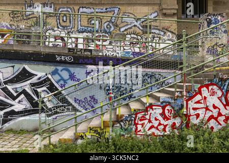 Several graffiti on a wall next to a staircase with green railings in an urban environment, Am Donaukanal Innere Stadt Wien Austria Stock Photo