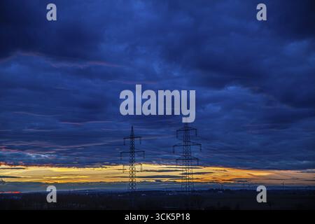 Electricity pylons in front of a colourful sunset and dramatic clouds Leitzerdorf Weinviertel Lower Austria Austria Stock Photo