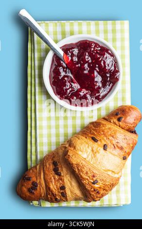 A delicious croissant with chocolate chips served alongside a bowl of berry jam on a checkered cloth. Stock Photo