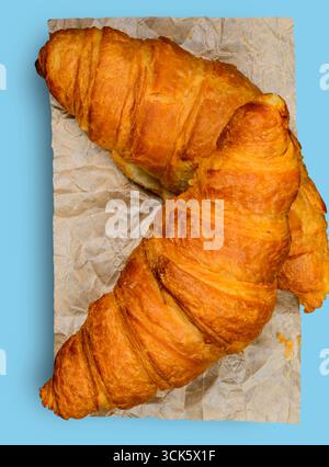 Two golden-brown croissants on crumpled parchment paper, showcasing their flaky texture and appetizing appearance. Stock Photo