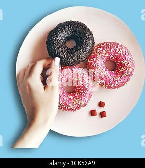 A hand reaching for colorful donuts on a pink plate, showcasing a delightful assortment of treats. Stock Photo