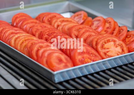 Freshly sliced tomatoes neatly arranged on a metal tray, ready for grilling Stock Photo